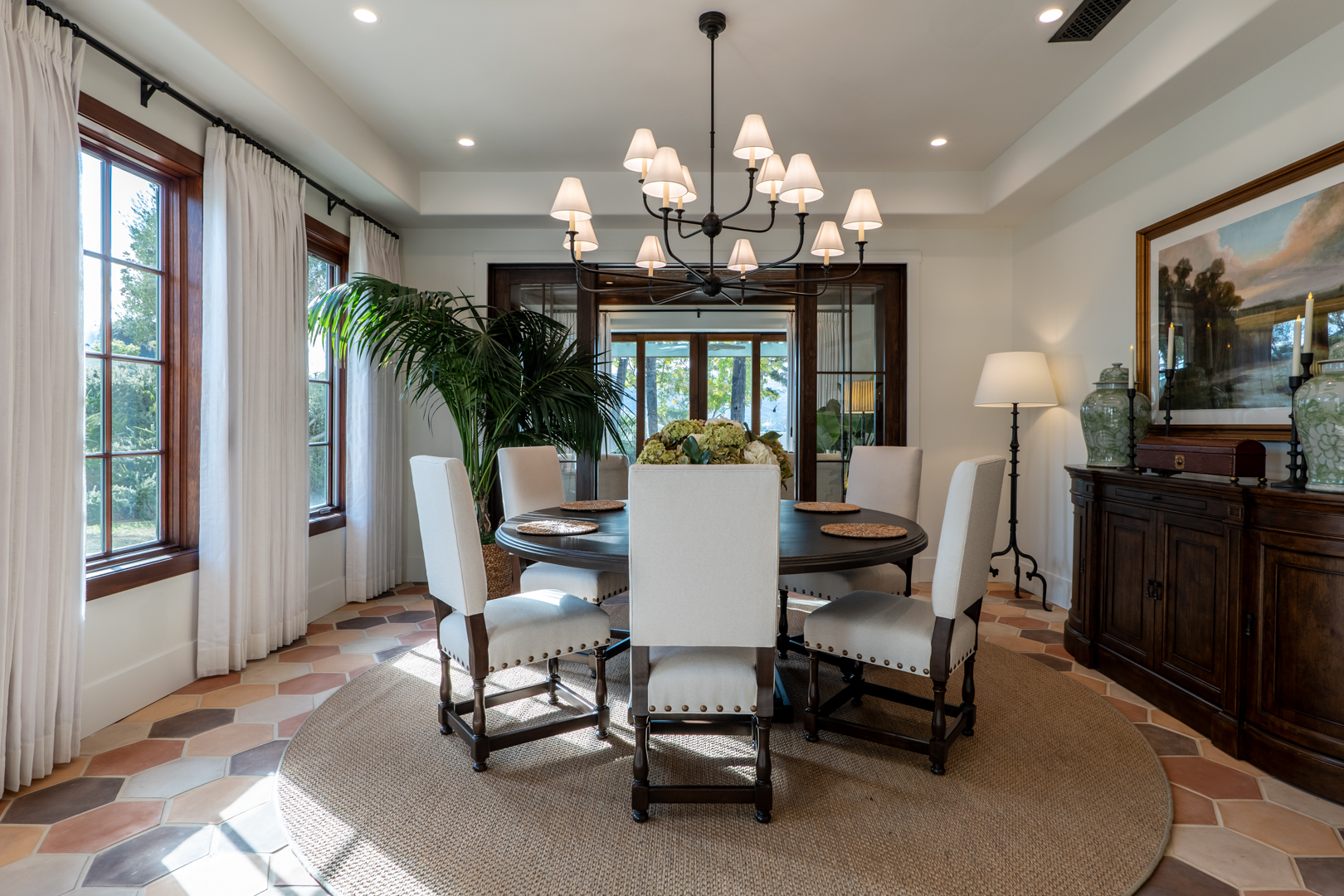 Luxury dining room with clay tile flooring, dark wood accents, and French doors opening to a sunroom